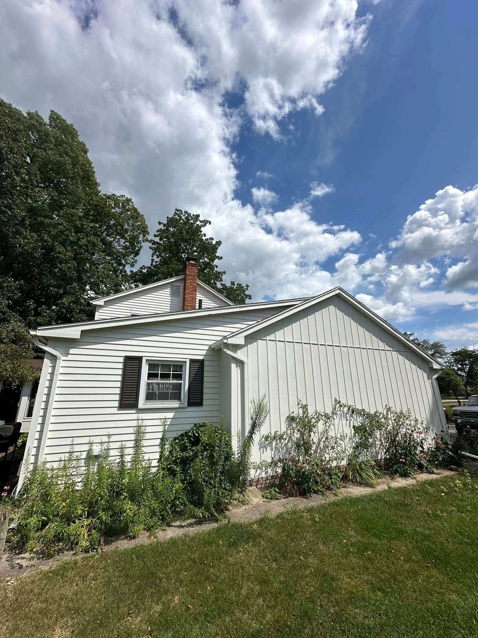 White house with a chimney and dark window under a blue sky with fluffy clouds.