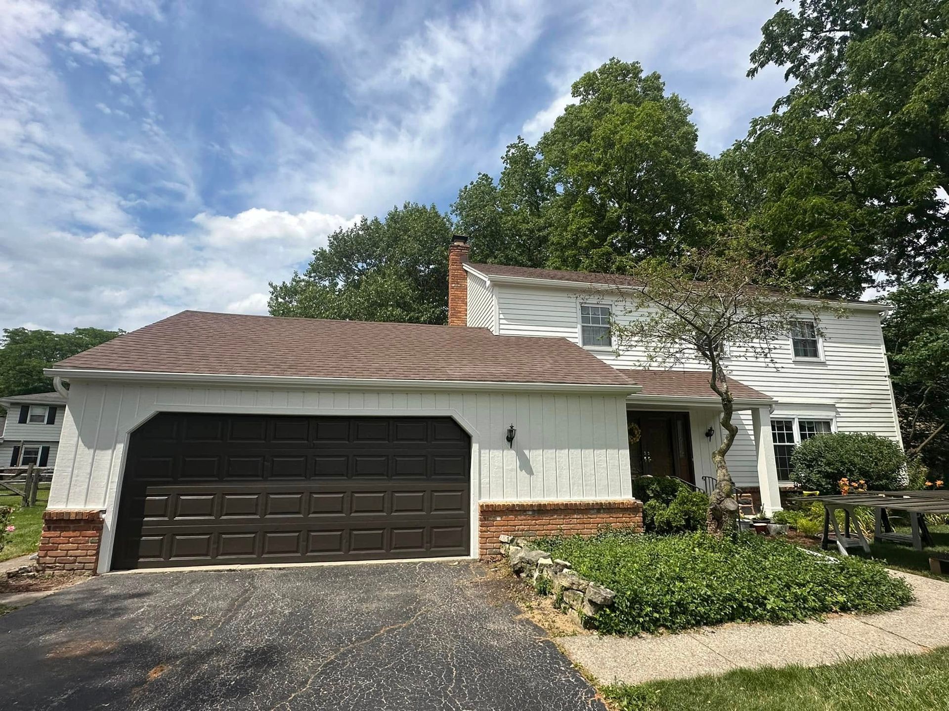 White house with brown roof and garage door; driveway and greenery in front.