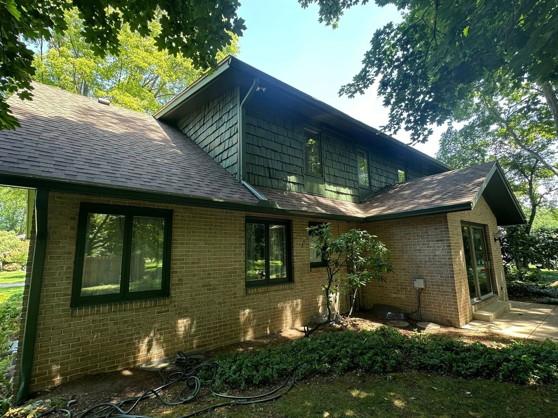 A two-story house with a brown roof and green siding, set in a yard with trees.