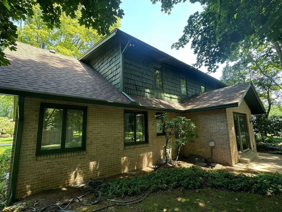 A two-story house with a brown roof and green siding, set in a yard with trees.