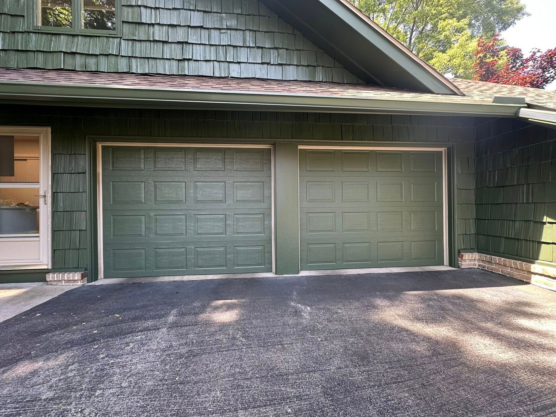Green garage doors on a house with dark asphalt driveway.
