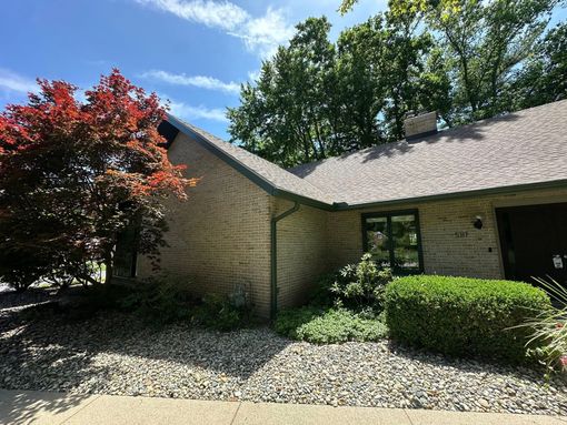Brick building with a dark green roof, surrounded by trees and a red-leaved bush. Blue sky above.