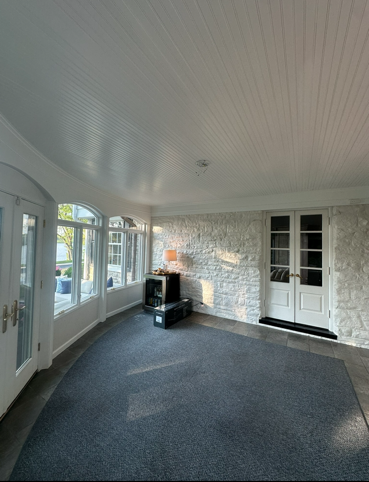 Gray house with white porch, in a yard with trees under a blue sky.