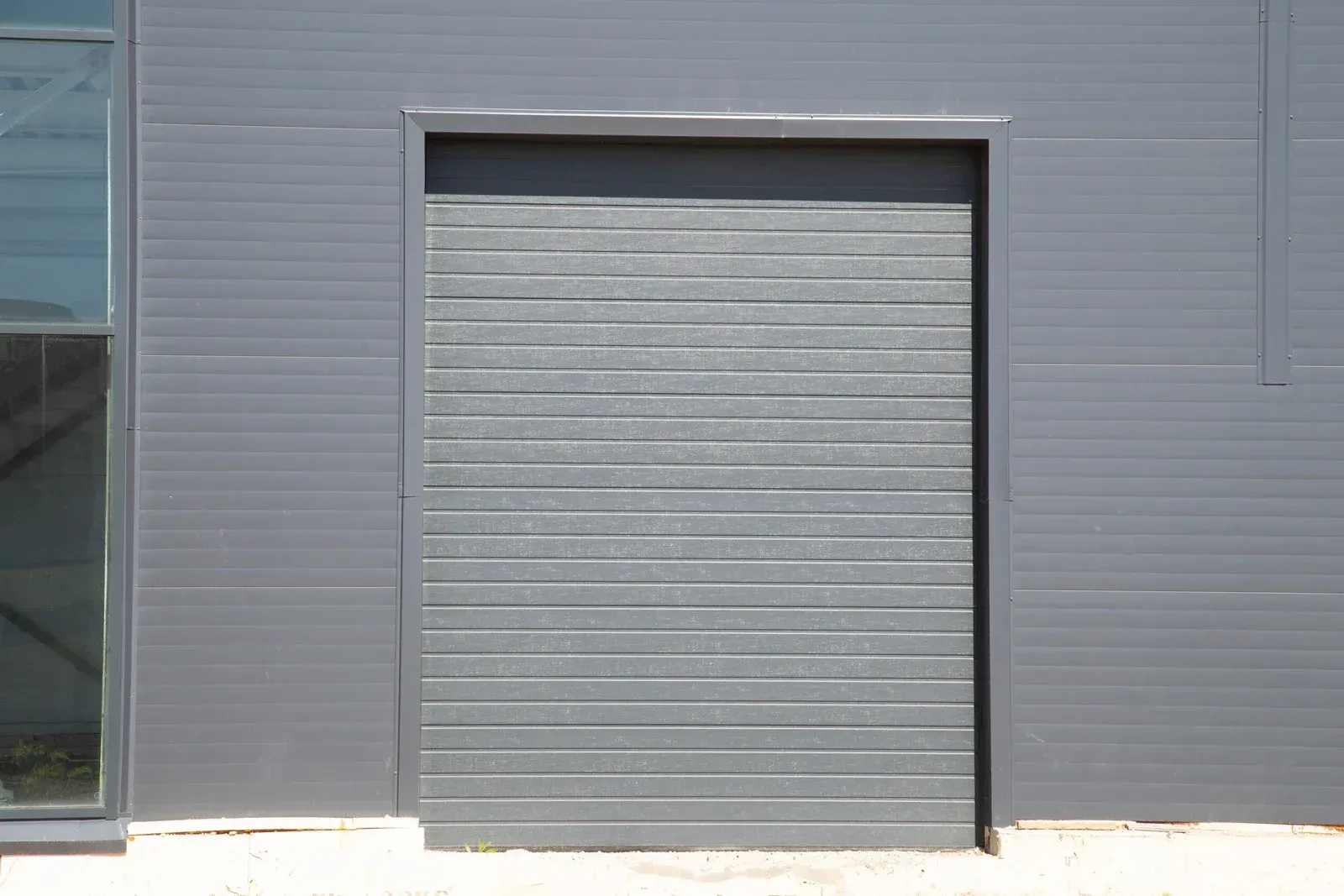 Two-story house with a white garage door, black asphalt driveway, and blue sky.