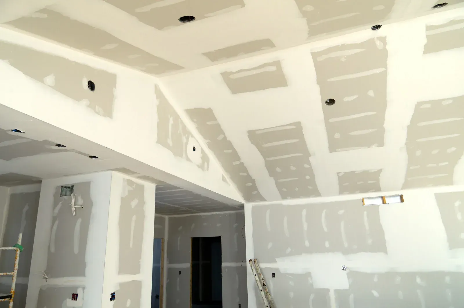Interior view of a room under construction with drywall installed on walls and ceiling.