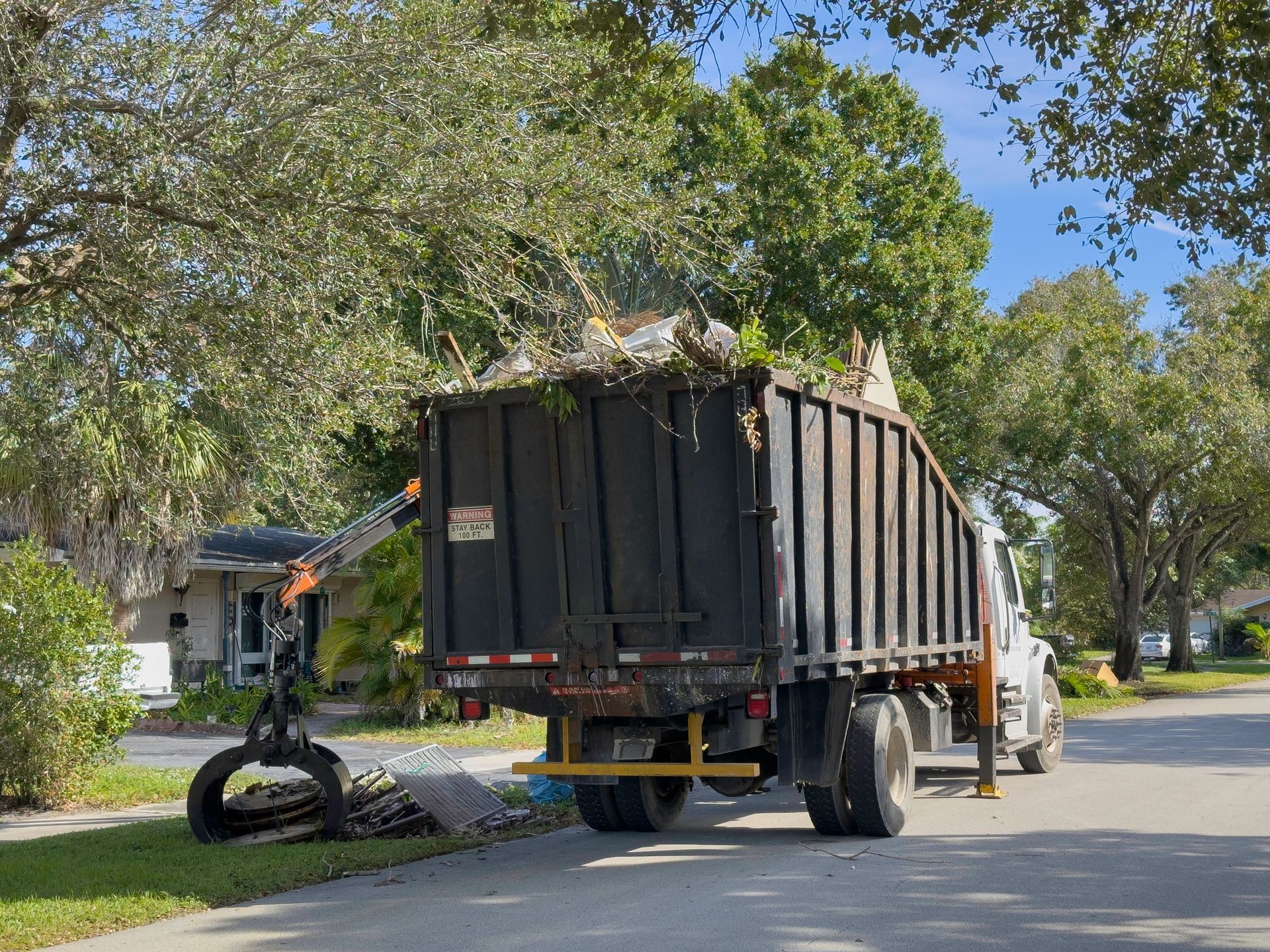 A dump truck is driving down a street with a crane attached to it.