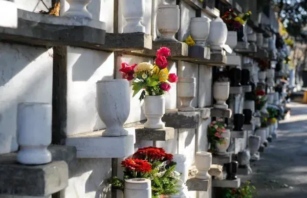 Rows of white marble tombs with vases holding colorful flowers, in a cemetery.