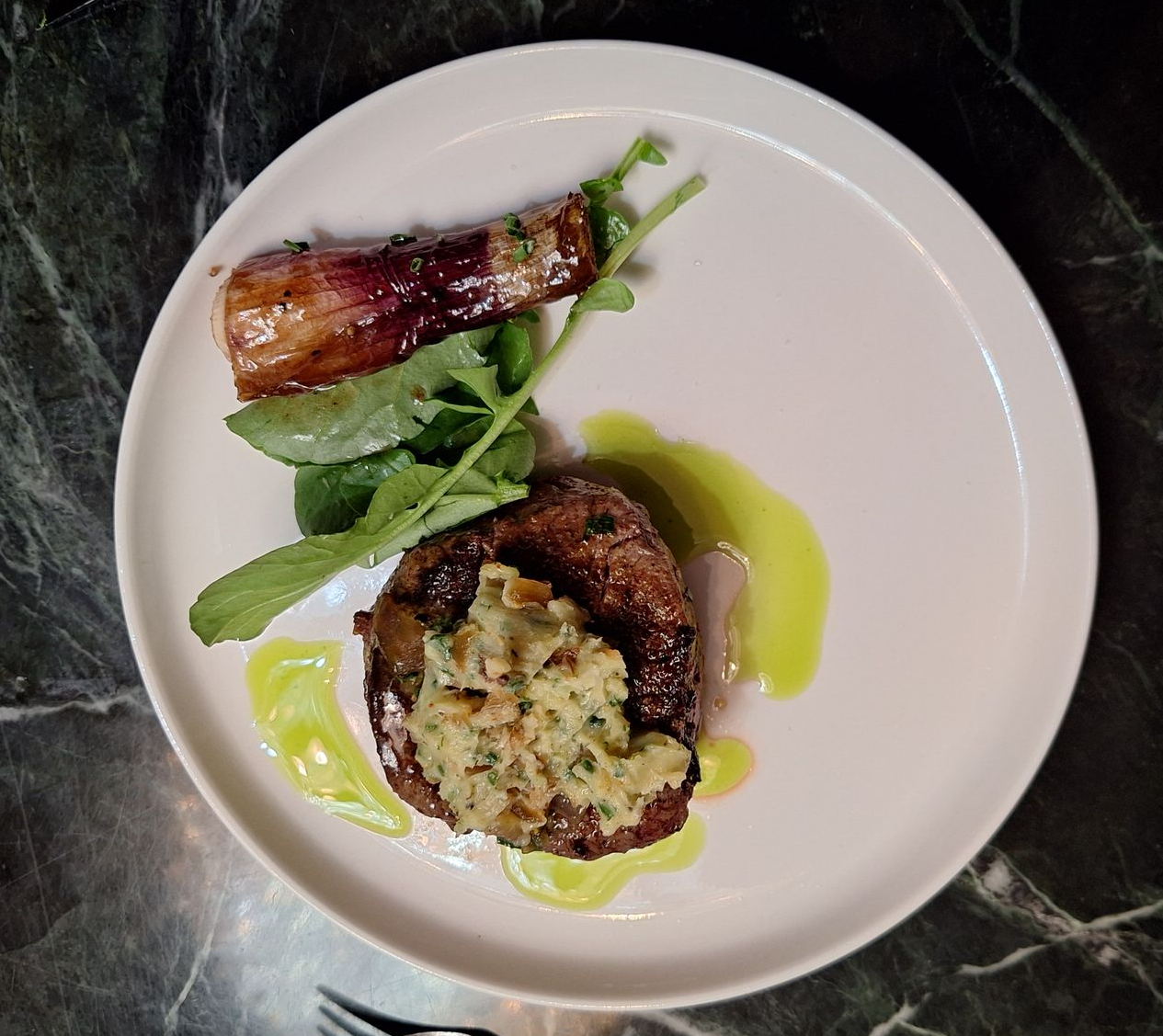 Steak dish on white plate: seared steak with avocado, red onion, arugula, and sauce.