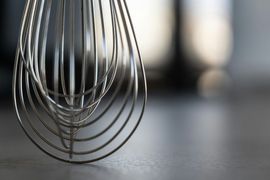 A close up of a wire whisk on a table.