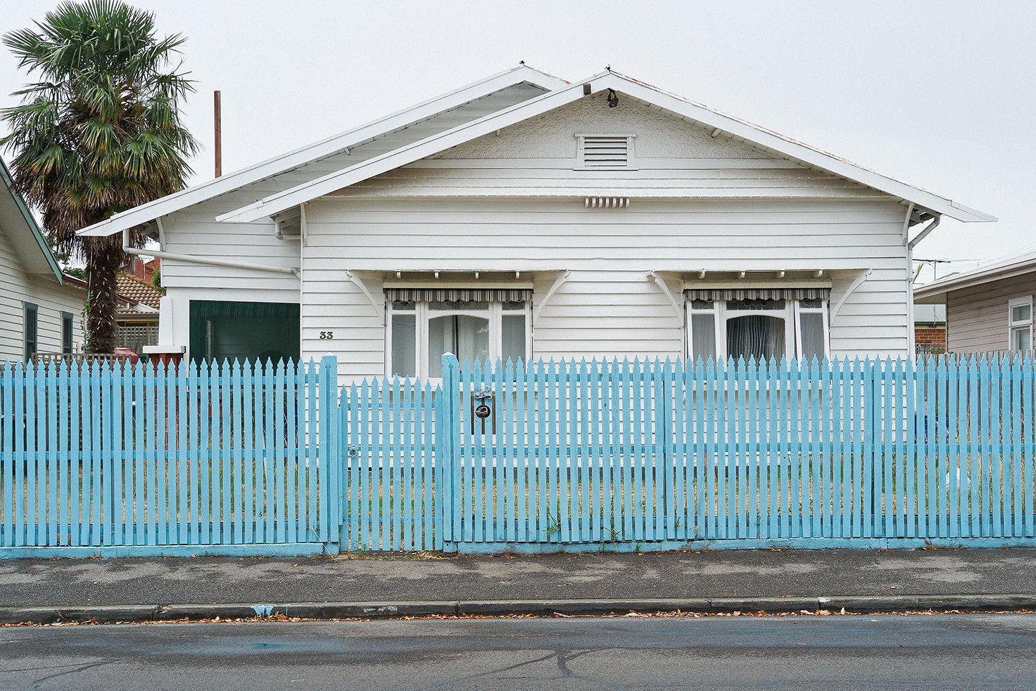 A suburban weatherboard house behind a blue picket fence.