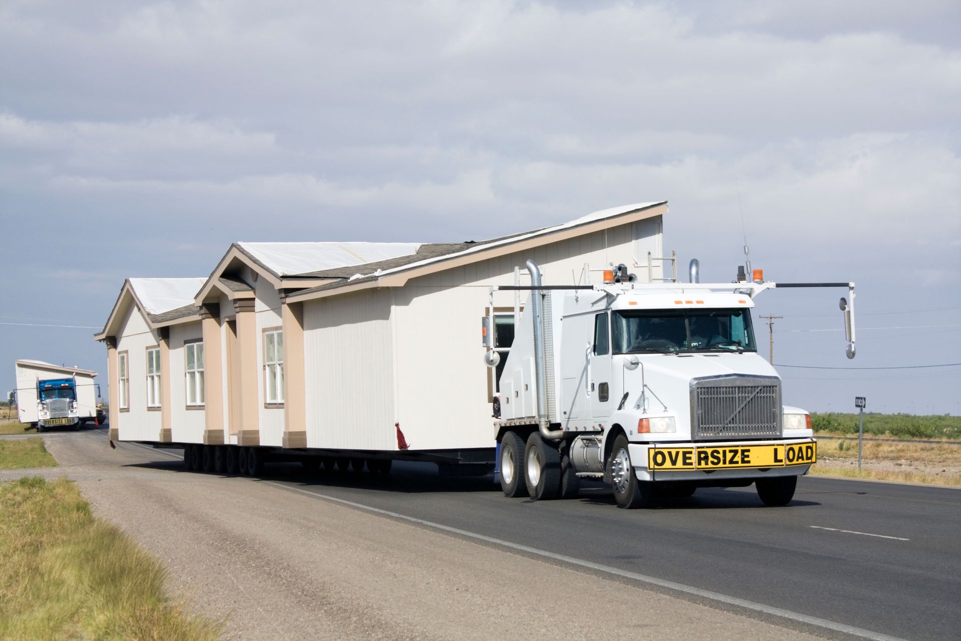 An oversize load truck is transporting a home on an open highway. An oversize load truck is transporting a home on an open highway.
