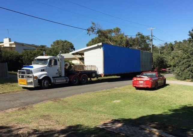 A white semi truck is carrying a mobile home down the road