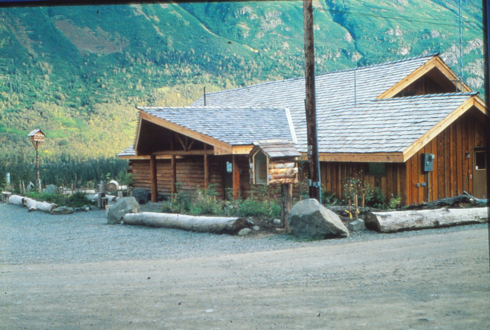 A large wooden house with a slate roof is surrounded by mountains