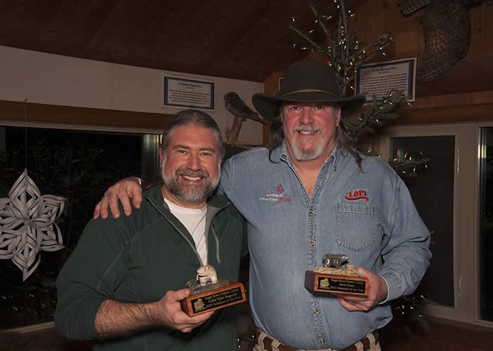 Two men are standing next to each other holding trophies.