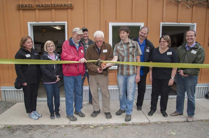 A group of people cutting a ribbon in front of a trail maintenance building