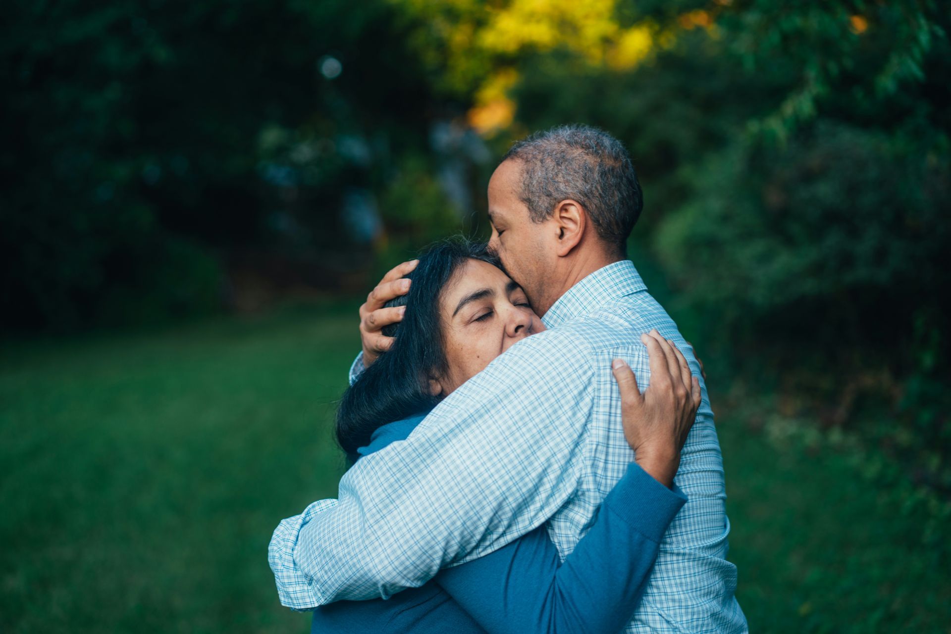 A man and a woman are hugging each other in a park.