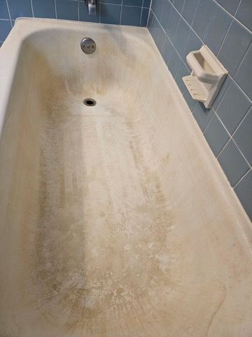 Dirty bathtub with brown stains and a soap holder. Blue tiled wall in the background.