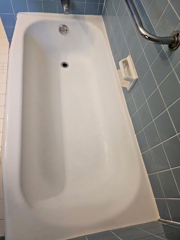 White bathtub with a drain, set against blue-tiled walls. A metal grab bar is visible.