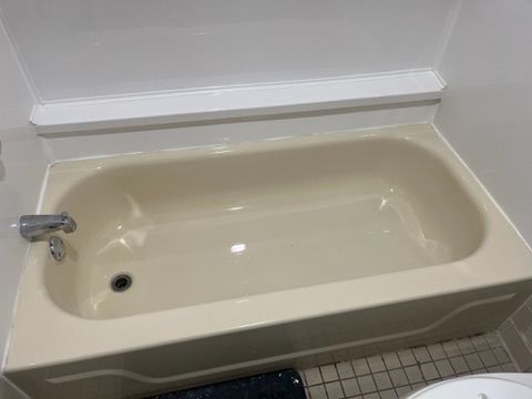 Beige bathtub with faucet in a bathroom, under a white ledge.