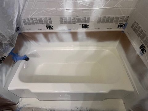 White bathtub in a room, taped and covered in plastic sheeting, likely for refinishing work.