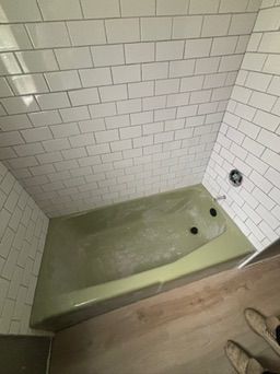 Green bathtub with white tile walls and a chrome faucet.