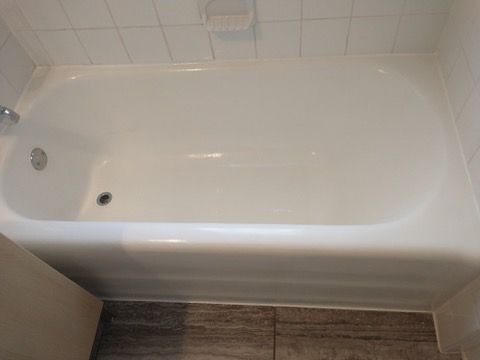 White bathtub with chrome fixtures and soap dish in a tiled bathroom.
