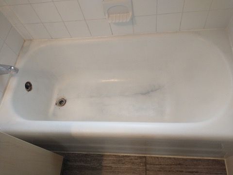 White bathtub with dark streaks, set in a bathroom with white tiled walls and a soap dish.