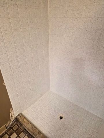 Empty white tiled shower stall with a corner drain.