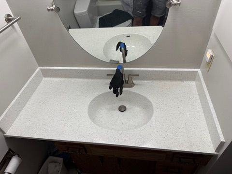 Bathroom vanity with white speckled countertop, oval sink, and round mirror.