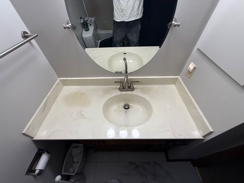 Bathroom vanity with oval mirror, white sink, and chrome faucet. Gray walls, and a person reflected in the mirror.