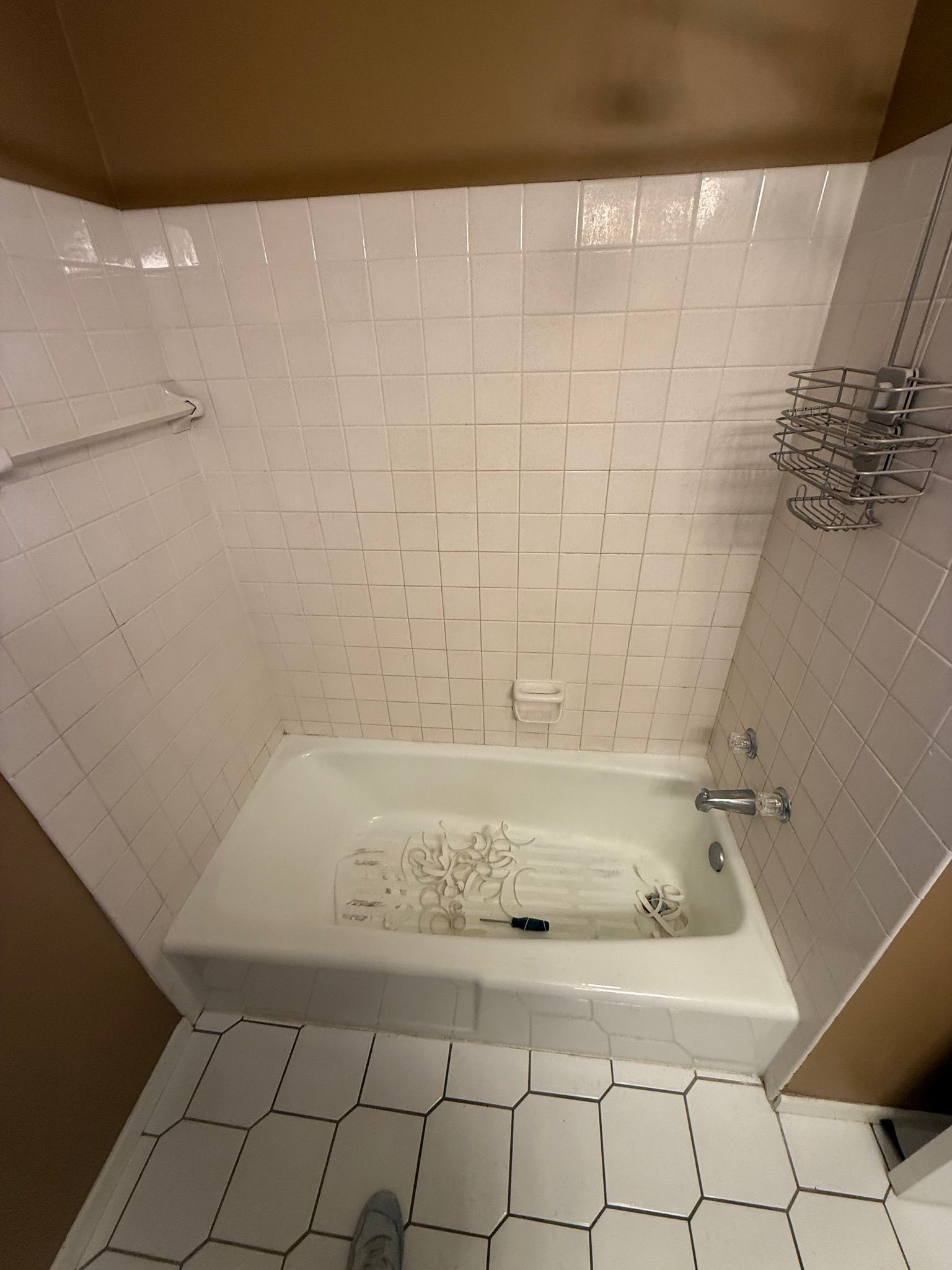 White tiled bathroom with a bathtub, fixtures, and a tiled floor.