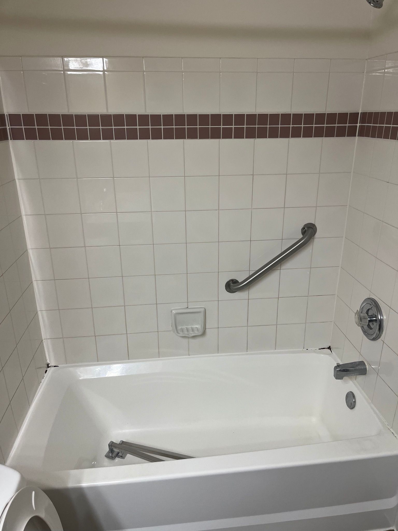 White bathtub with tiled walls and a grab bar.