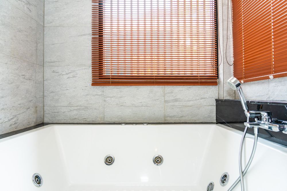 A white jacuzzi tub with jets, next to a window with brown wooden blinds.