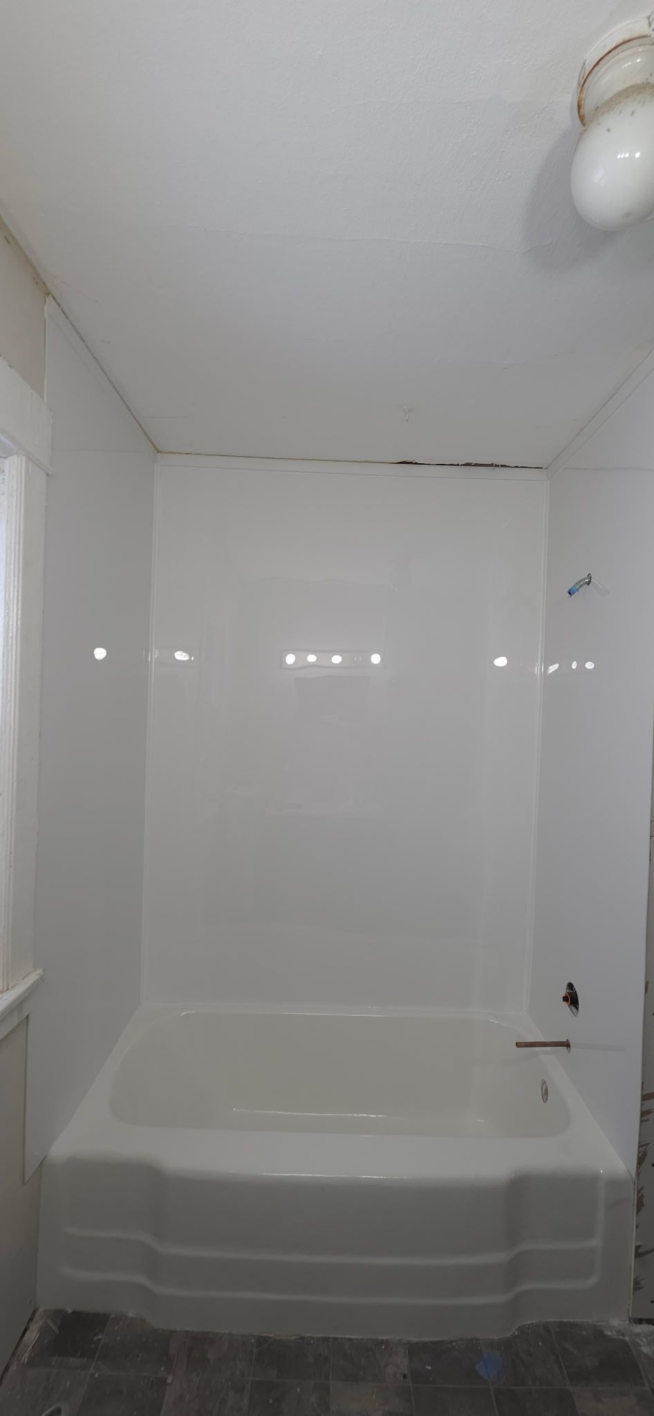 Bathroom with a white bathtub and shower surround, light gray floor, and a ceiling light.