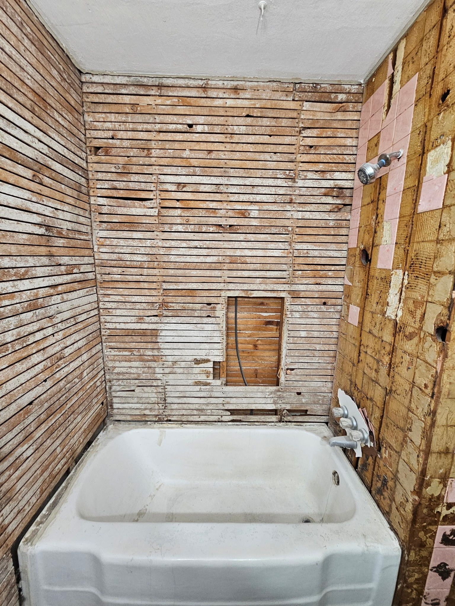 Bathroom renovation, showing a bathtub, exposed wood lath walls, and shower fixture.