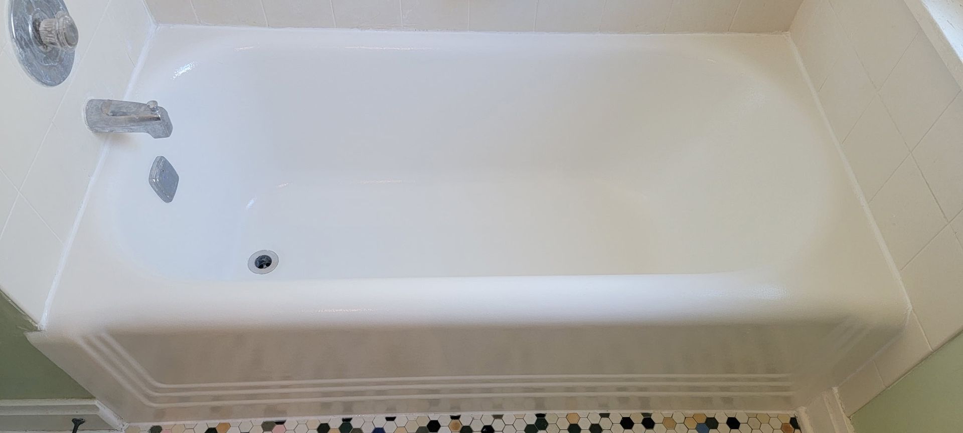 White bathtub in a bathroom with chrome fixtures and patterned tile trim.