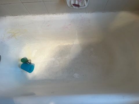 Bathtub with soap residue, stains, and a blue cup.