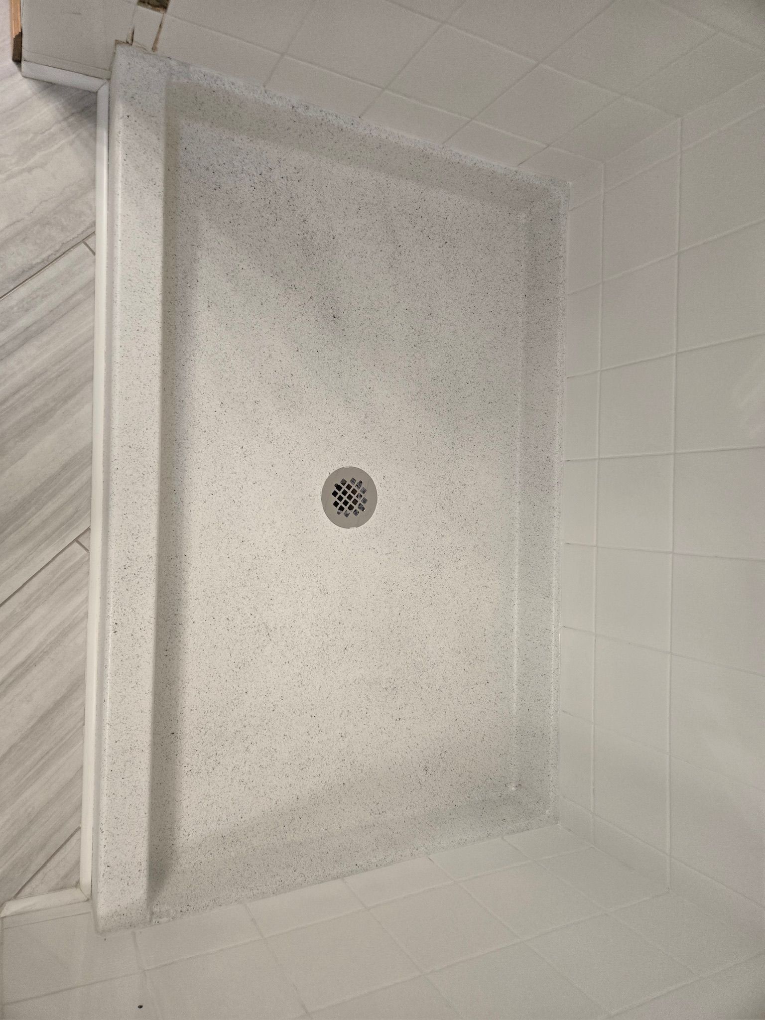 Shower stall with white speckled walls, drain, and tiled wall.