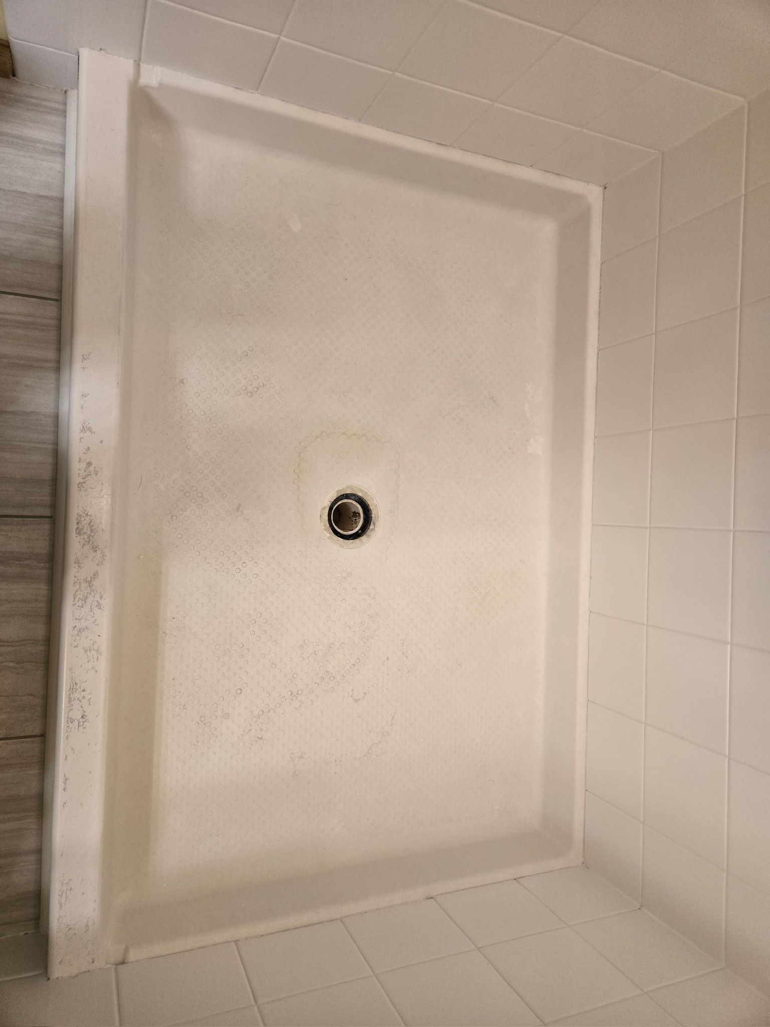 White shower base with central drain, surrounded by white tile walls.