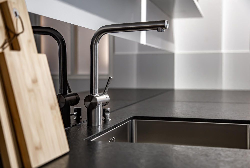 Stainless steel kitchen faucet and sink on dark countertop; wooden cutting board.