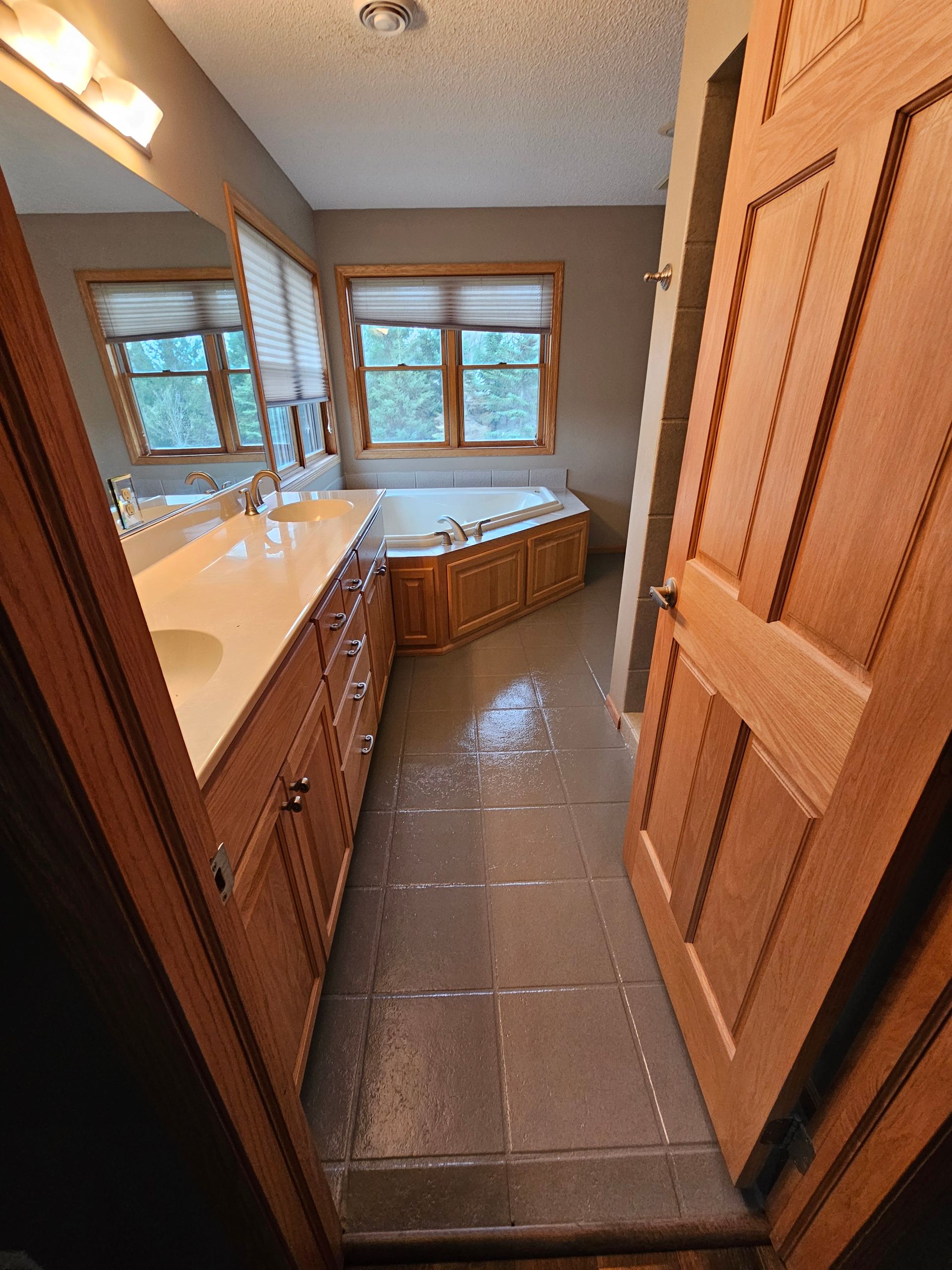 Bathroom with wooden cabinets, beige countertop, and a built-in tub near windows.