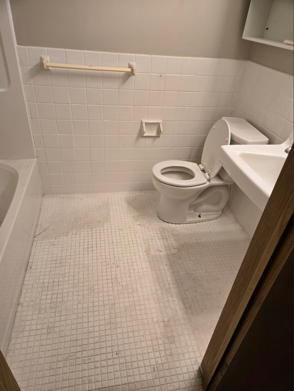 Small bathroom with white tiled floor and walls; toilet, sink, and tub visible.