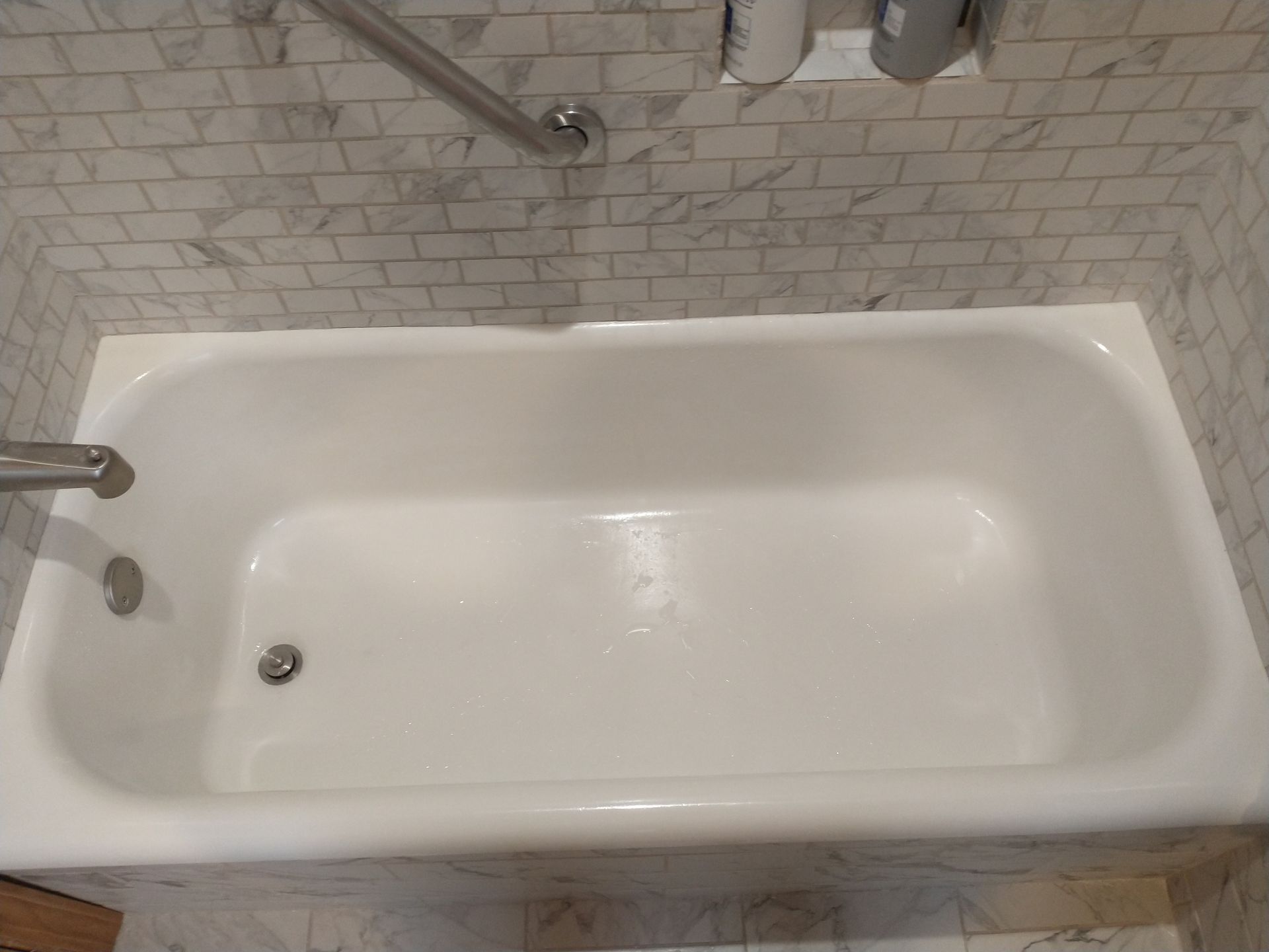 White bathtub in bathroom with marble-tiled walls and a silver grab bar.