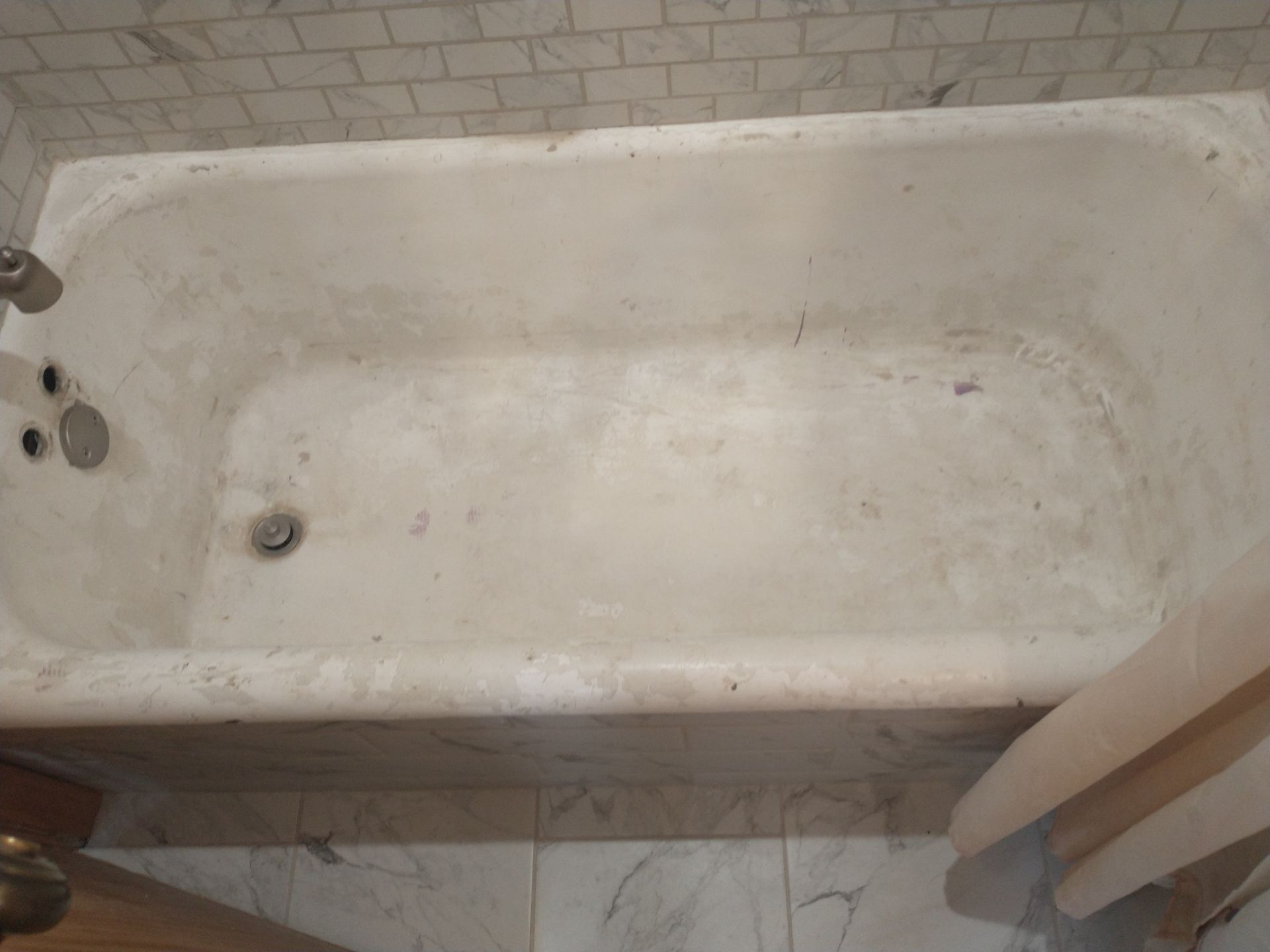 Dirty, off-white bathtub with staining. Surrounded by marble tile.