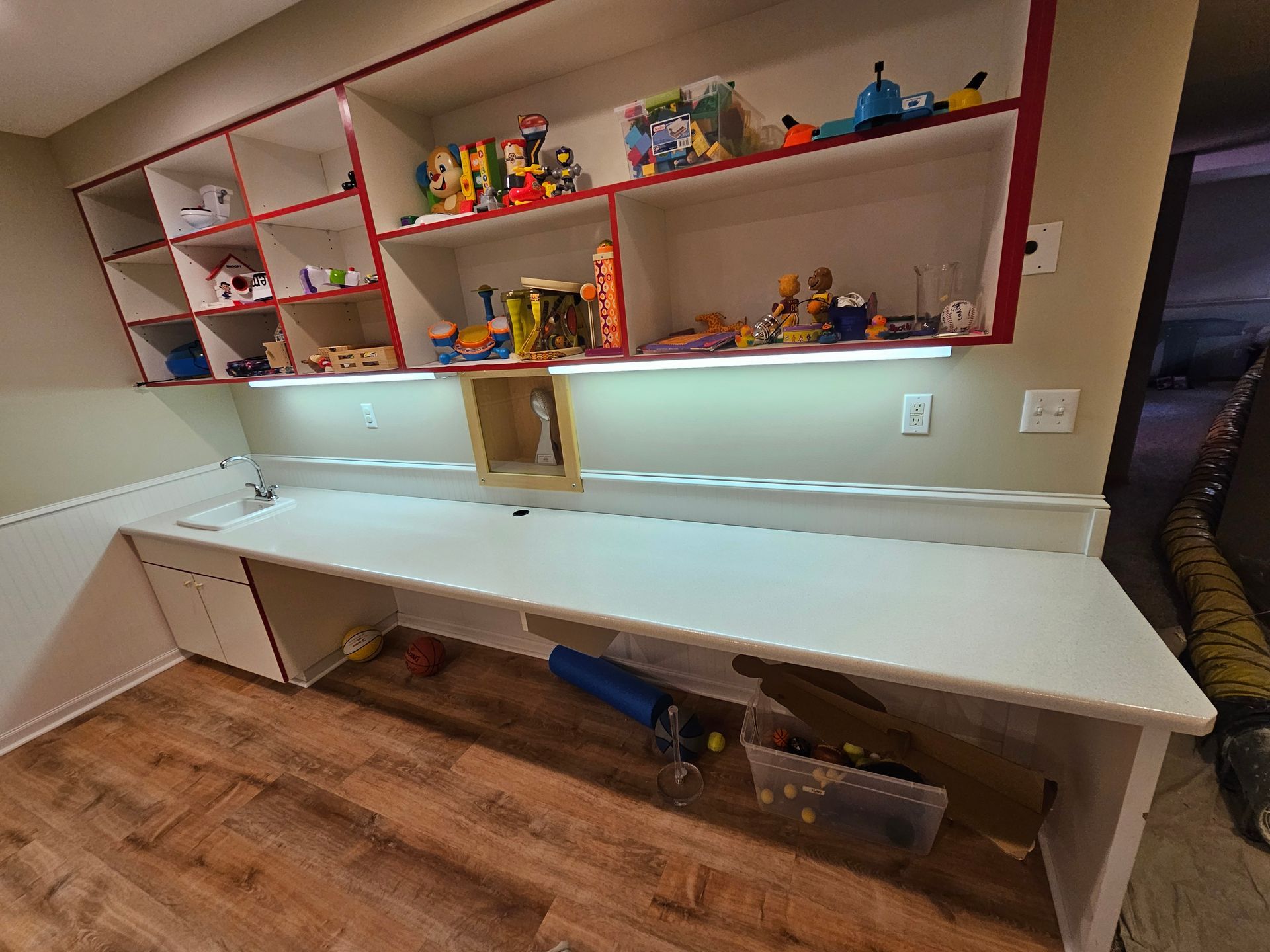 Built-in desk with shelves above, holding toys and books. The desk has a white surface and is set in a room with wood floors.