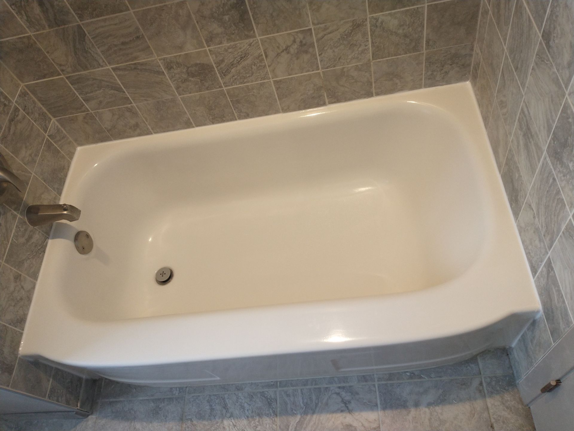 White bathtub with chrome fixtures, surrounded by gray tile.