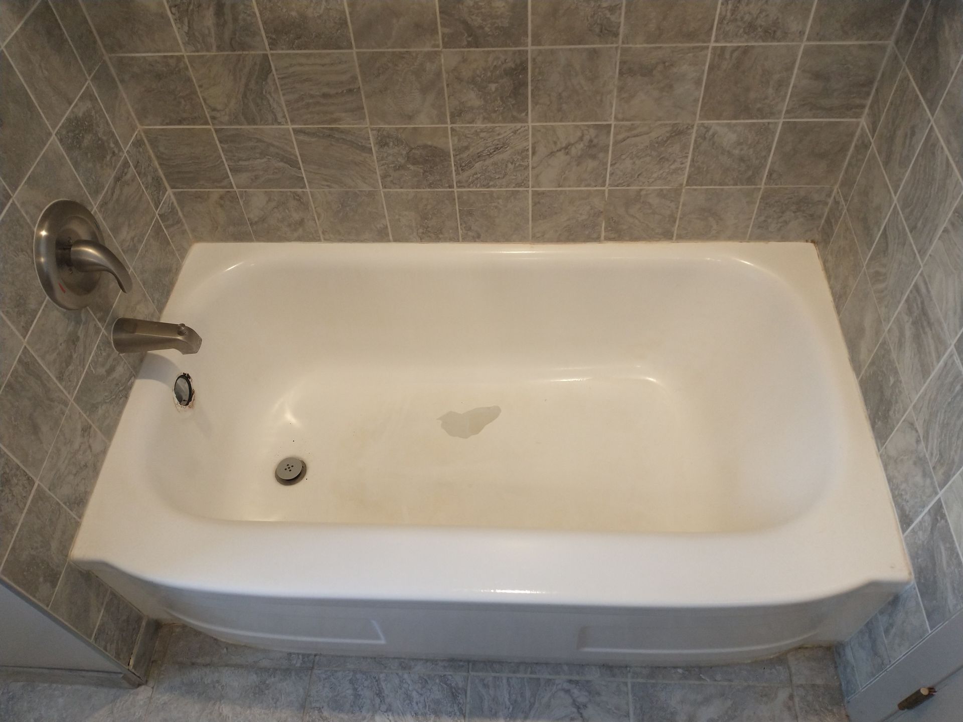 White bathtub with silver faucet, set in a tiled alcove.