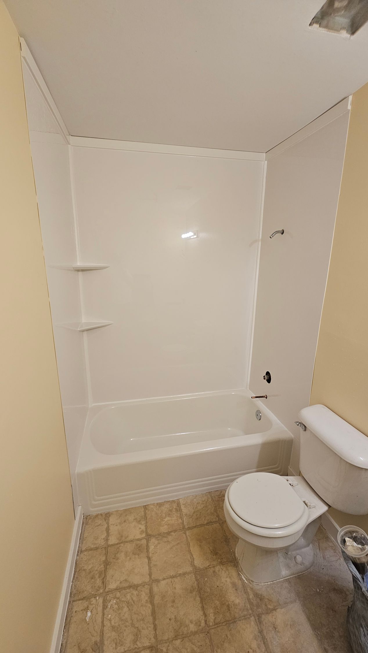 Bathroom with a white bathtub and walls. A toilet is in the foreground. Yellow wall on either side.