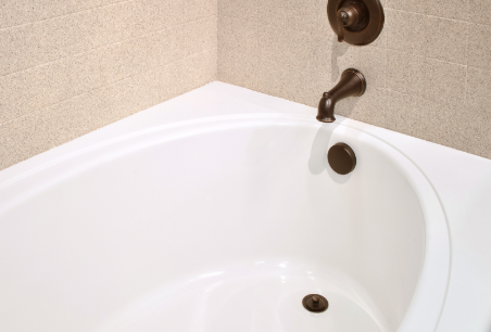 White bathtub with bronze fixtures in a bathroom corner.