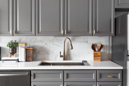 Gray kitchen cabinets with a white countertop and marble backsplash.
